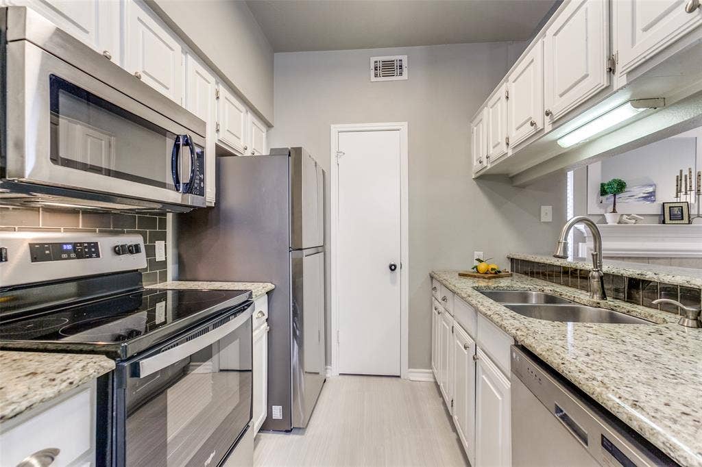 Kitchen featuring stainless steel appliances, stone-pattern countertops, white cabinetry, a dual-basin undermount sink, and tiled backsplash