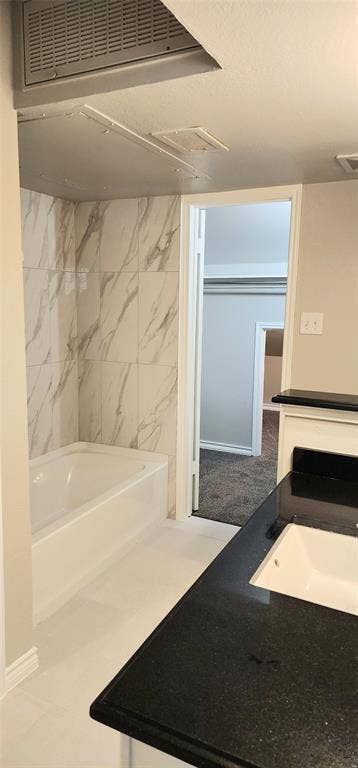 Bathtub enclosure featuring white and tile with grey veining, contrasting black countertop, and recessed vanity sink