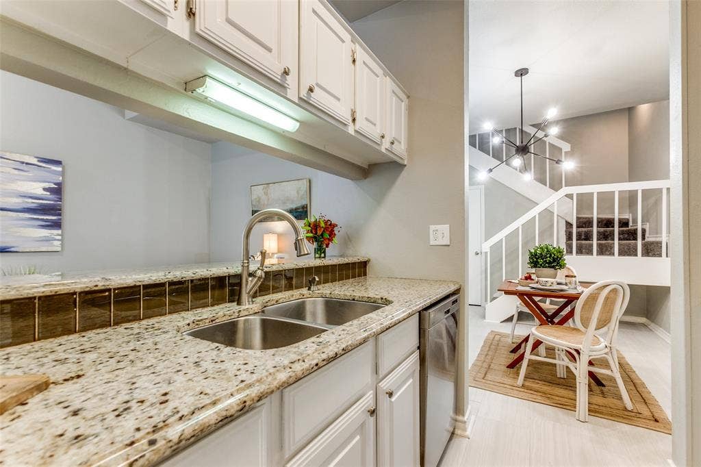 Kitchen featuring white cabinetry, stone-finish countertops, an undermount dual-basin stainless steel sink with a pull-down faucet, and brown tile backsplash