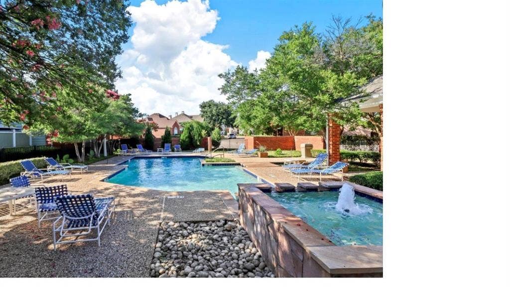 Outdoor pool area featuring a stone-clad spa with a fountain feature, pebbled hardscaping, masonry perimeter wall, and mature landscaping