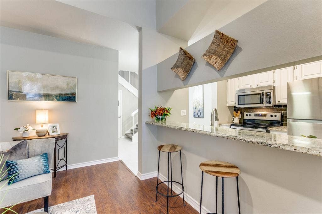 Pass-through breakfast bar with stone-surfaced countertop, white cabinetry, integrated stainless steel appliances, and wood-finish flooring