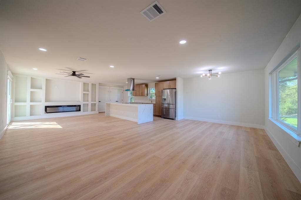 Open-concept interior featuring light wood-finish flooring, recessed lighting, built-in wall cabinetry, a stone-surround fireplace, and a kitchen island with a waterfall-edge countertop