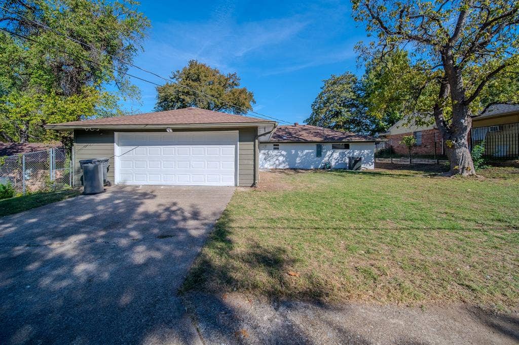 Exterior featuring a detached garage with horizontal siding, concrete driveway, and expansive lawn with mature trees
