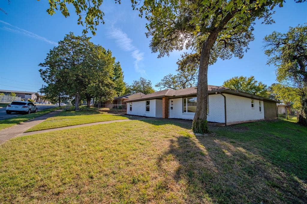 Single-story brick exterior featuring a low-slope roof and expansive corner lot with mature shade trees