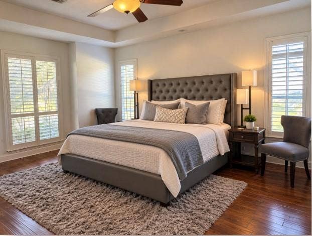 Tray ceiling with a central ceiling fan, hardwood flooring, and white plantation shutters