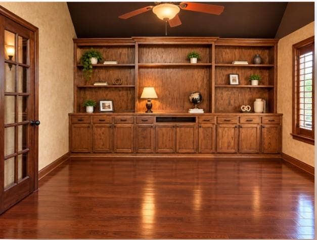 Custom floor-to-ceiling wood cabinetry with integrated shelving and base storage, hardwood flooring, vaulted ceiling, French doors, and wooden plantation shutters.