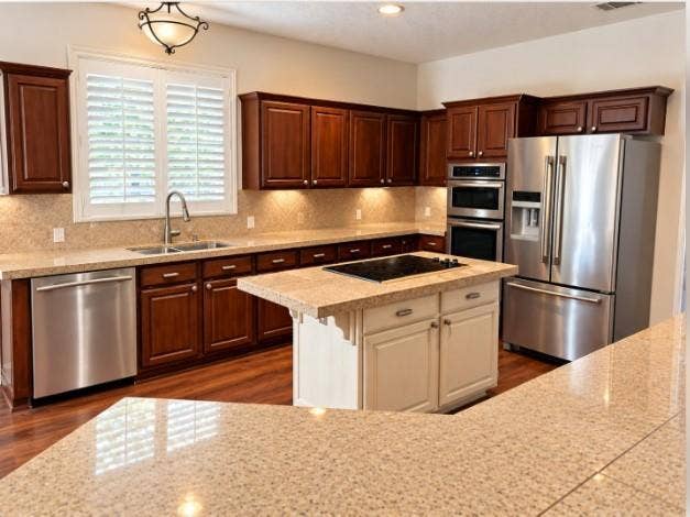 Kitchen featuring stained wood cabinetry, a central island with a contrasting finish, granite countertops, built-in stainless steel appliances, and hardwood flooring.