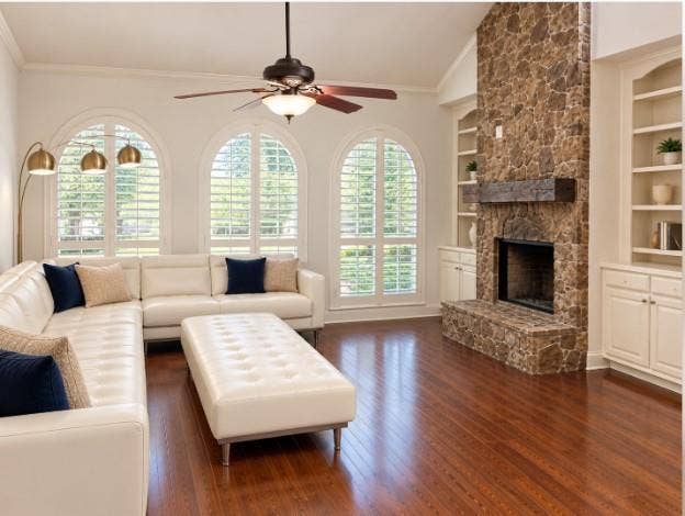 Floor-to-ceiling stone fireplace with a timber mantel, flanked by custom built-in cabinetry, hardwood flooring, vaulted ceilings, and Plantation Shutters!