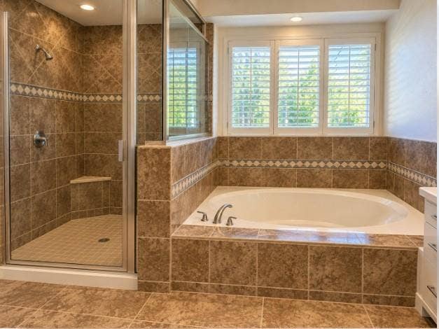 Soaking tub with a tile surround, glass-enclosed shower featuring a built-in bench, decorative mosaic tile accents, and plantation shutters