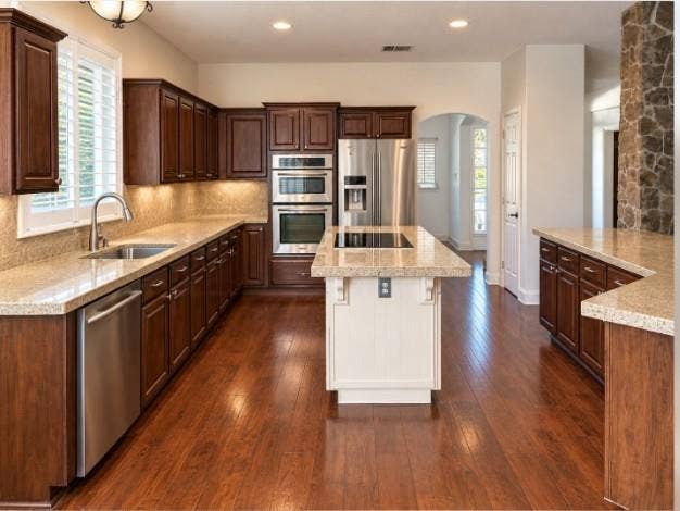 Kitchen featuring stained wood cabinetry, a central island with a contrasting finish, granite countertops, built-in stainless steel appliances, and hardwood flooring.