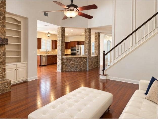 Floor-to-ceiling stone fireplace with a timber mantel, flanked by custom built-in cabinetry, hardwood flooring, vaulted ceilings, and Plantation Shutters! Open to Kitchen.