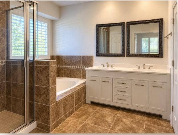New Dual-sink vanity with a solid-surface countertop, tile-surrounded soaking tub, glass-enclosed shower, and tile flooring.