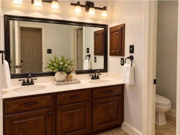 Bathroom #2 - Double vanity featuring dark-stained wood cabinetry, matte black widespread faucets, and a framed mirror with integrated six-light overhead fixture.