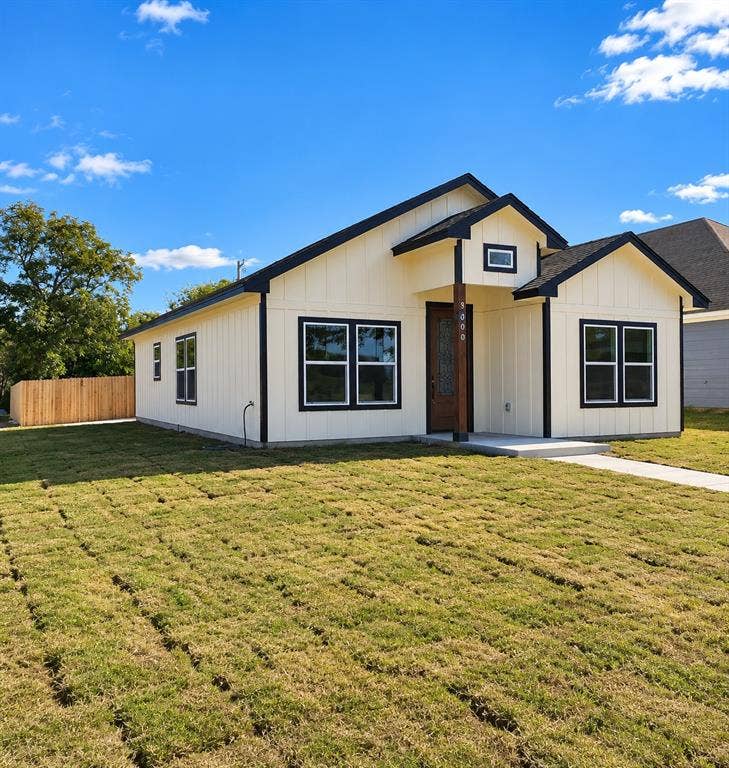 Single-story exterior featuring board-and-batten siding, contrasting dark window trim, a covered entry with wood-post detailing, and a fenced yard