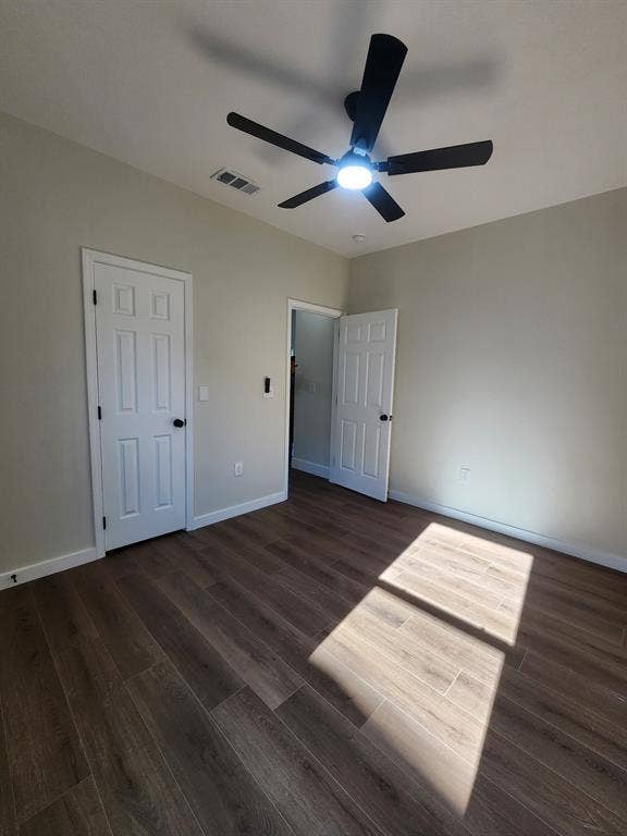Neutral-toned interior featuring wood-finish flooring, two six-panel interior doors, and a ceiling-mounted fan with an integrated light fixture
