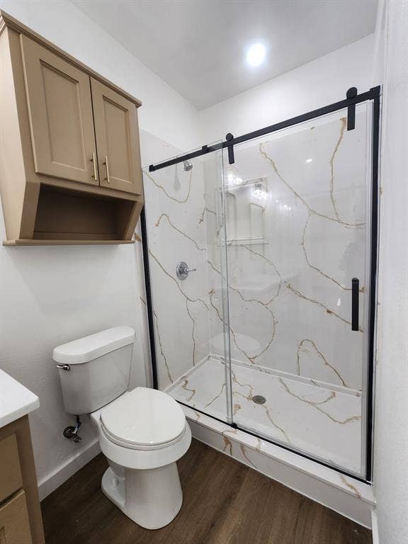 Walk-in shower with stone-finish surround, sliding glass door, black hardware, wall-mounted cabinetry, and wood-finish flooring