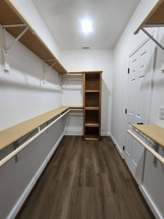 Walk-in closet featuring wood-finish flooring, built-in wooden shelving, and wall-mounted shelving units