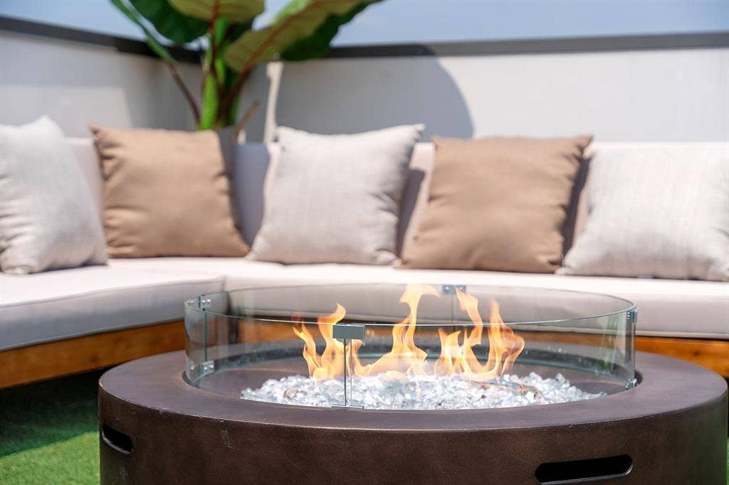 Circular fire pit featuring a smooth dark-toned base, integrated glass wind guard, and decorative stone filler