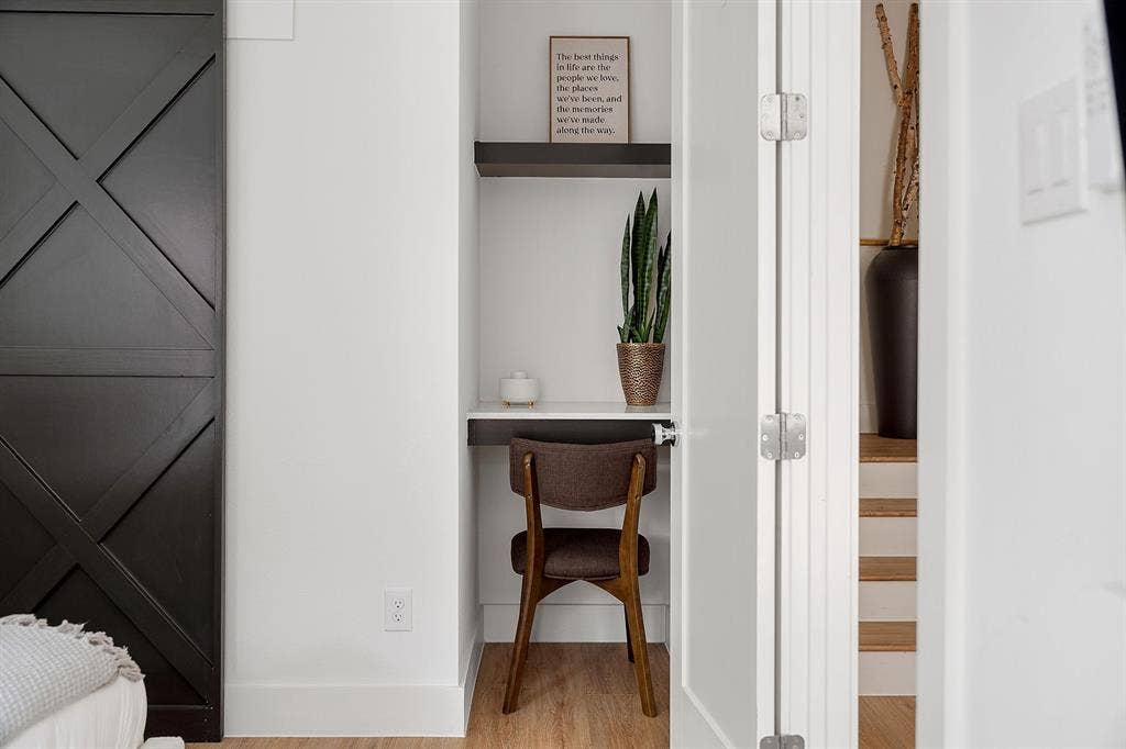 Built-in alcove featuring a floating desk, overhead shelving, wood-finish flooring, and a sliding barn-style door with a cross-brace design