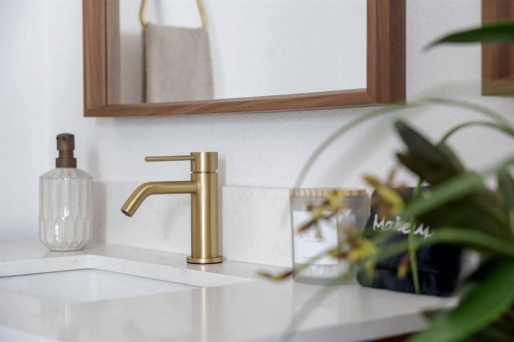 Modern vanity featuring a stone-composite countertop, undermount sink, brass single-handle faucet, and wood-framed mirror