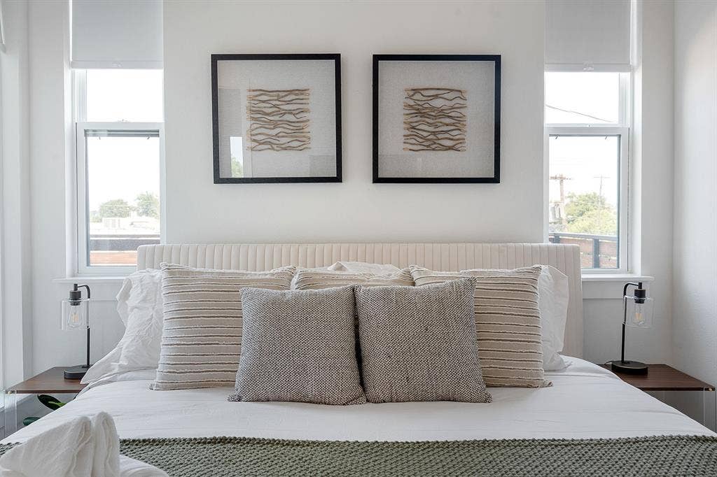Dual vertical windows with roller shades, complemented by wall-mounted lighting fixtures on fixed wooden bedside platforms