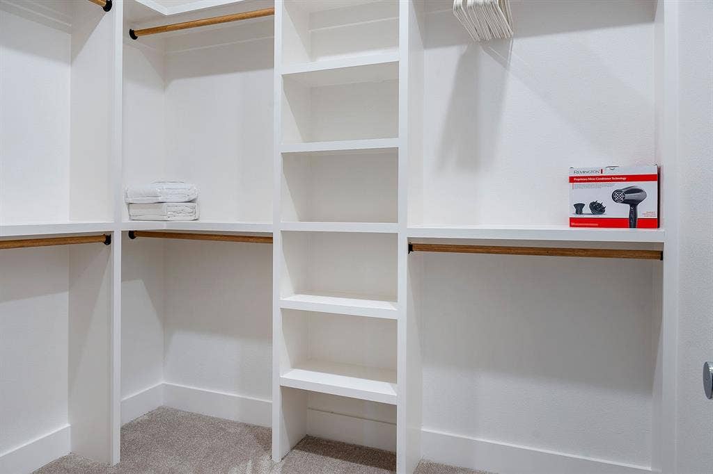 Walk-in closet featuring white built-in shelving, multiple hanging rods, and neutral carpeting