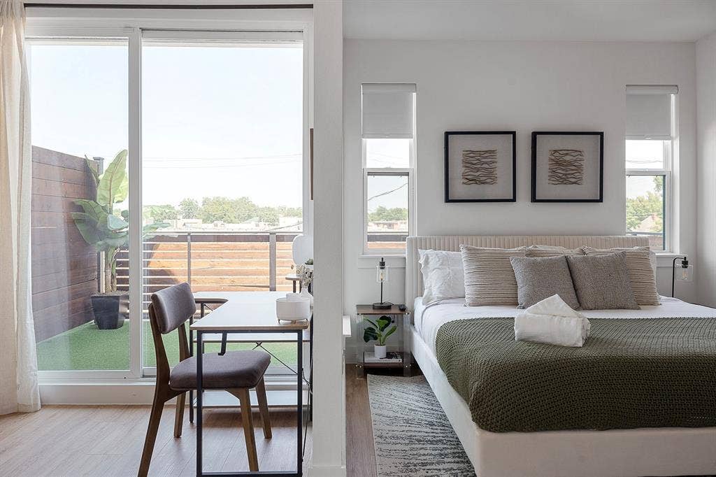 Sliding glass doors opening to a private balcony with horizontal wood slat fencing and artificial turf, complemented by wood-finish flooring and dual double-pane windows