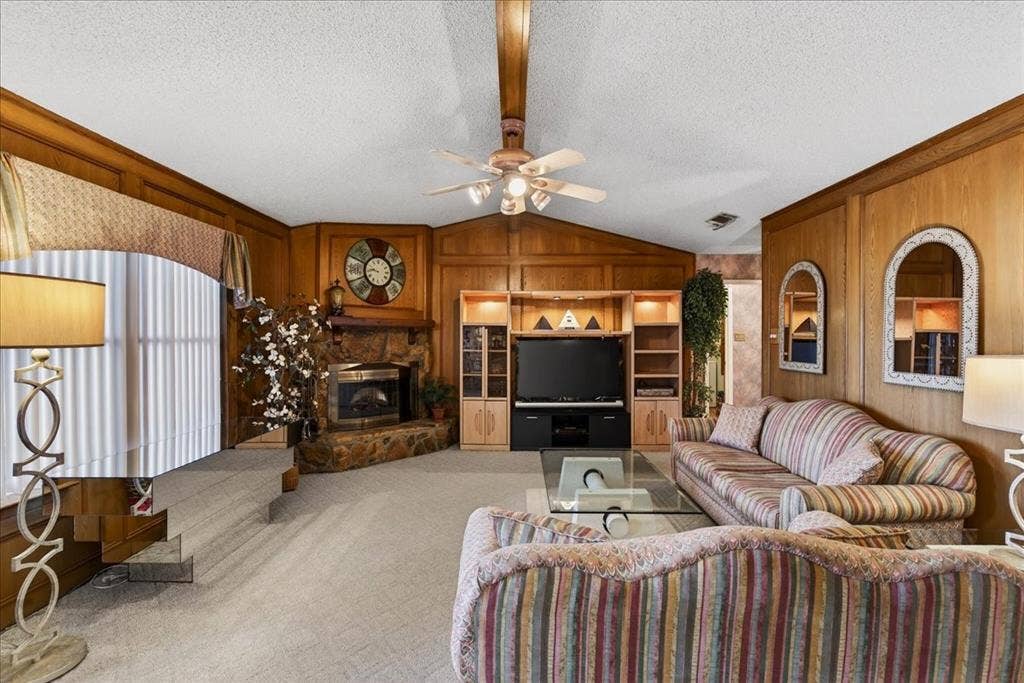 10118 Lakeview Street, Payne Springs, TX 75156 Vaulted ceilings with a central ceiling fan, wood-paneled walls, stone-faced fireplace, and built-in media cabinetry