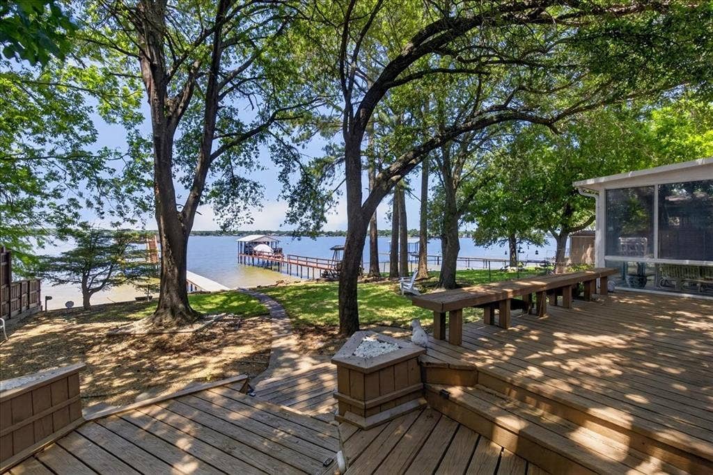 10118 Lakeview Street, Payne Springs, TX 75156 Multi-level wood deck featuring built-in bench seating, a stone-accented fire feature, mature trees, and a private dock extending into the water
