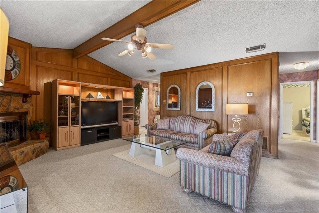 10118 Lakeview Street, Payne Springs, TX 75156 Living room featuring vaulted ceilings with exposed wood beams, wood-paneled walls, a stone-surround fireplace, and custom built-in cabinetry