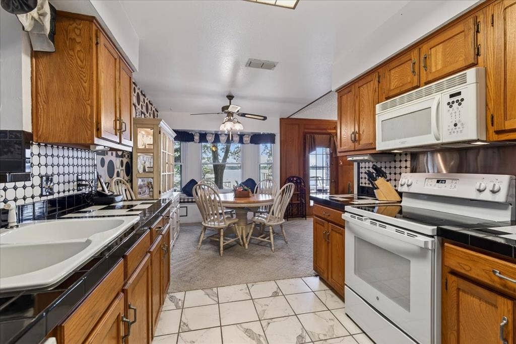 10118 Lakeview Street, Payne Springs, TX 75156 Kitchen featuring wood cabinetry, white appliance suite, geometric patterned tile backsplash, dark countertops, and integrated tile flooring
