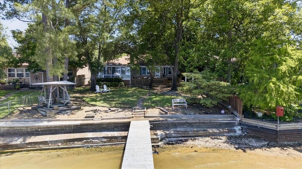 10118 Lakeview Street, Payne Springs, TX 75156 Waterfront property featuring a private wooden pier, tiered stone bulkheading, mature trees, and a landscaped yard