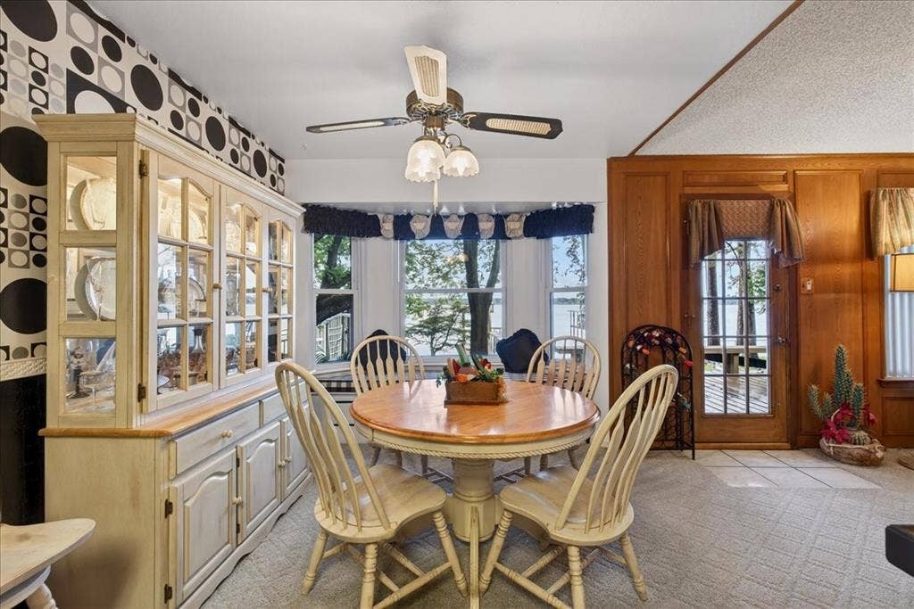 10118 Lakeview Street, Payne Springs, TX 75156 Dining area featuring a built-in floor-to-ceiling hutch, bay windows, wood-paneled walls, a glass-paneled exterior door, and a ceiling fan with integrated lighting