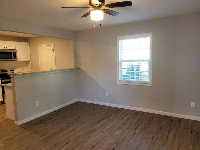 Interior space featuring wood-finish flooring, a ceiling fan with integrated lighting, a single-hung window, and a pass-through breakfast bar with a stone-surfaced countertop