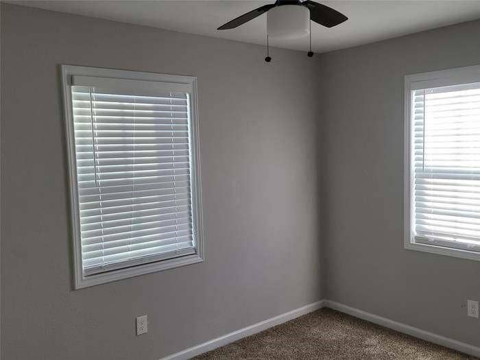 Neutral-toned interior walls, dual windows featuring horizontal blinds, and a ceiling-mounted light fixture with a fan
