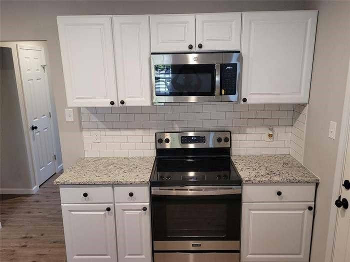 Kitchen featuring white shaker-style cabinetry, speckled stone-finish countertops, stainless steel microwave, stainless steel range, and subway tile backsplash