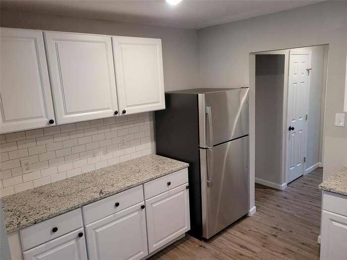 Kitchen featuring white shaker-style cabinetry, stone-finish countertops, subway tile backsplash, stainless steel refrigerator, and wood-finish flooring