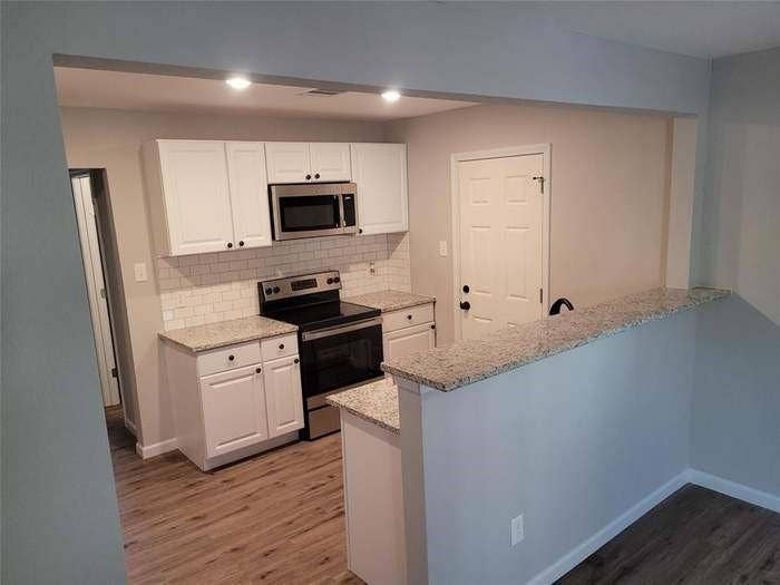 Kitchen featuring white shaker-style cabinetry, stone-finish countertops, subway tile backsplash, stainless steel appliances, and wood-finish flooring