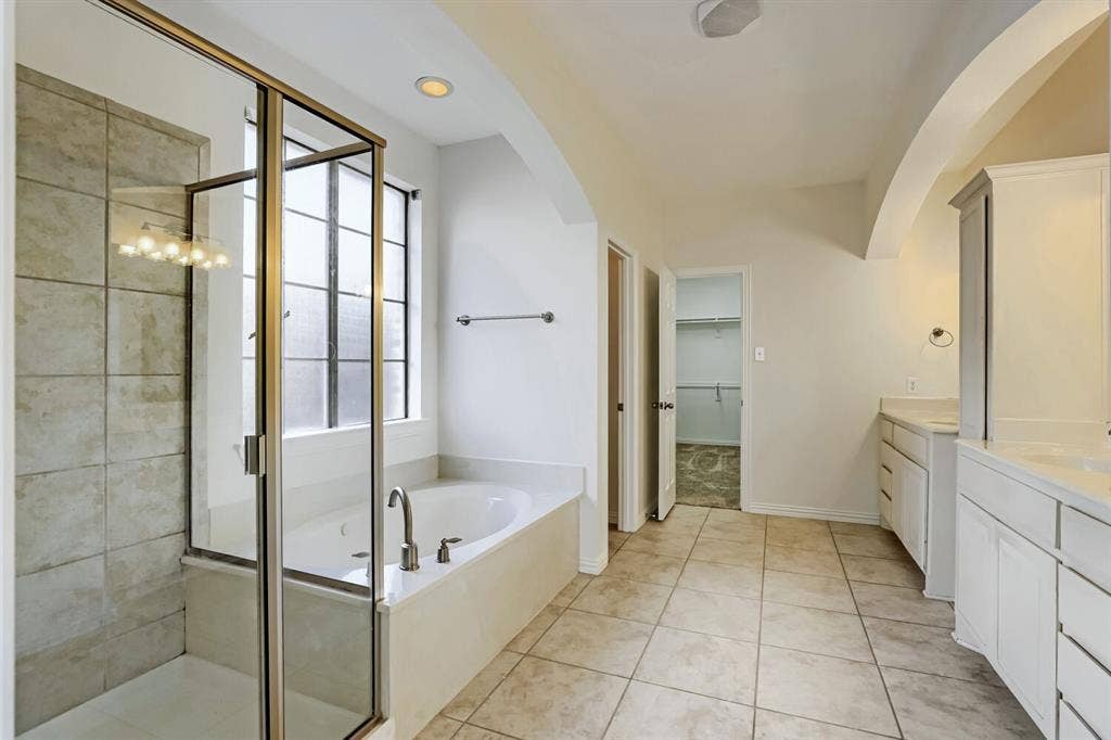 7013 Salem Court, Rowlett, TX 75089 Bathroom featuring a glass-enclosed shower with tile surround, a built-in soaking tub, a dual-sink vanity with white cabinetry, and ceramic tile flooring