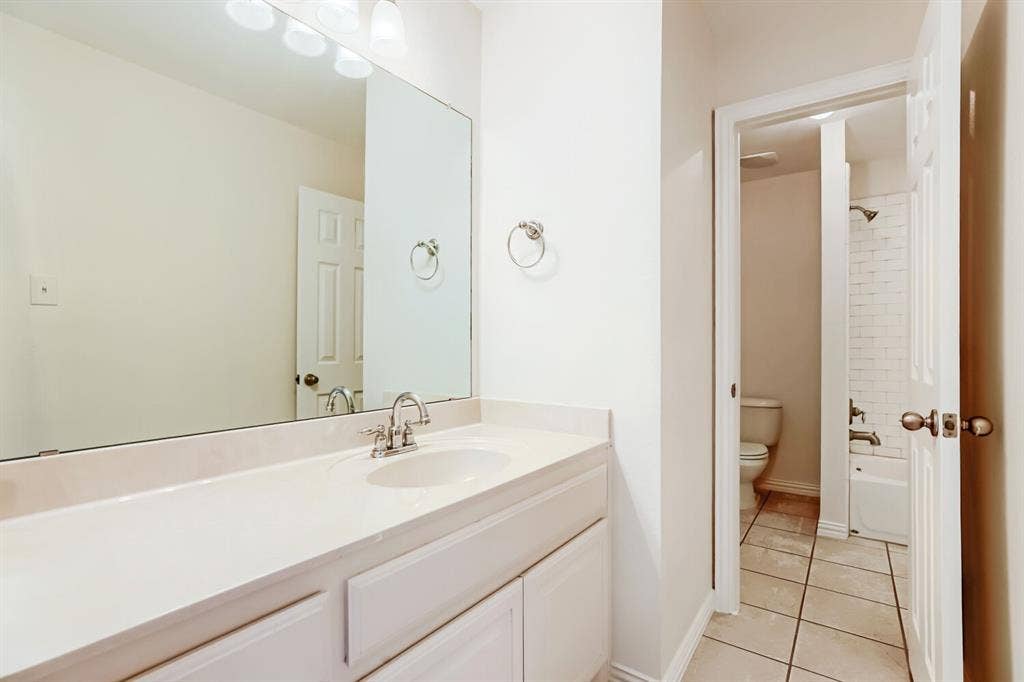 7013 Salem Court, Rowlett, TX 75089 Vanity featuring a solid-surface countertop with an integrated basin, large wall-mounted mirror, polished chrome faucet, tile flooring, and a shower-tub combination with white subway-style wall tile