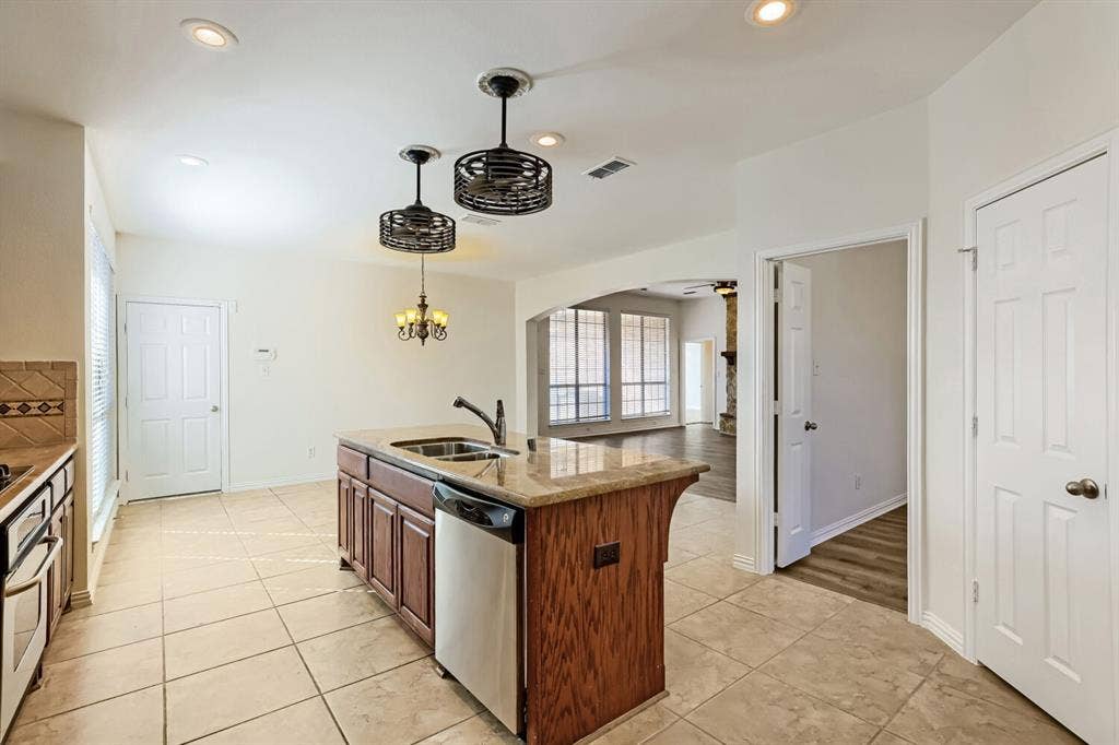 7013 Salem Court, Rowlett, TX 75089 Kitchen island featuring a stone countertop, under-mount stainless steel sink, and wood cabinetry