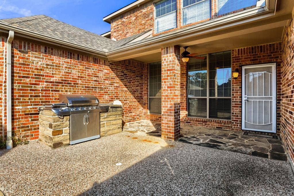 7013 Salem Court, Rowlett, TX 75089 Covered brick patio featuring a built-in stainless steel grill with stone masonry surround, flagstone accents, ceiling fan, and exterior wall-mounted lighting