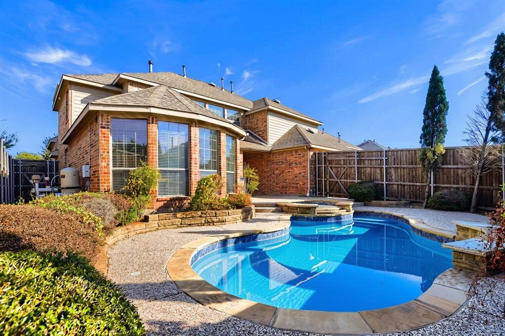 7013 Salem Court, Rowlett, TX 75089 Brick exterior with a multi-gabled roofline, featuring an in-ground swimming pool with an integrated spa, stone coping, and a surrounding concrete patio