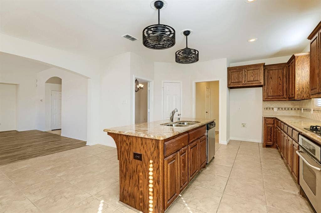 7013 Salem Court, Rowlett, TX 75089 Kitchen featuring a center island, stone-finish countertops, stainless steel integrated dishwasher, custom wood-finish cabinetry, and industrial-style dual pendant light fixtures