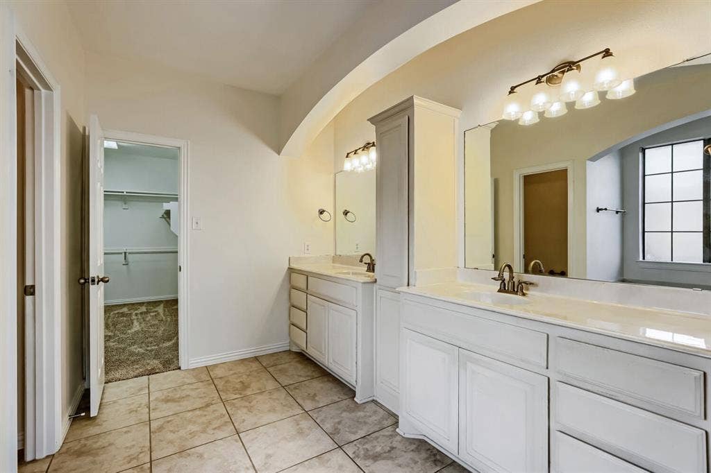 7013 Salem Court, Rowlett, TX 75089 Dual vanity featuring white cabinetry, stone-finish countertops, undermount sinks, and wall-mounted lighting fixtures