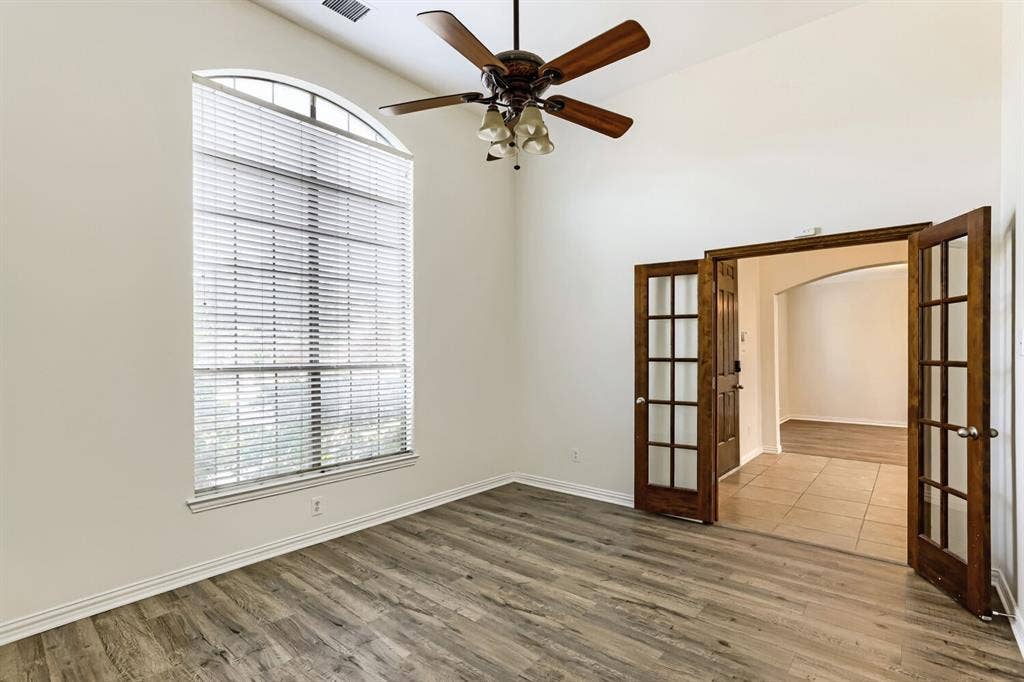 7013 Salem Court, Rowlett, TX 75089 High-ceilinged room featuring wood-finish flooring, an arched window, a ceiling fan with integrated lighting, and stained wood French doors