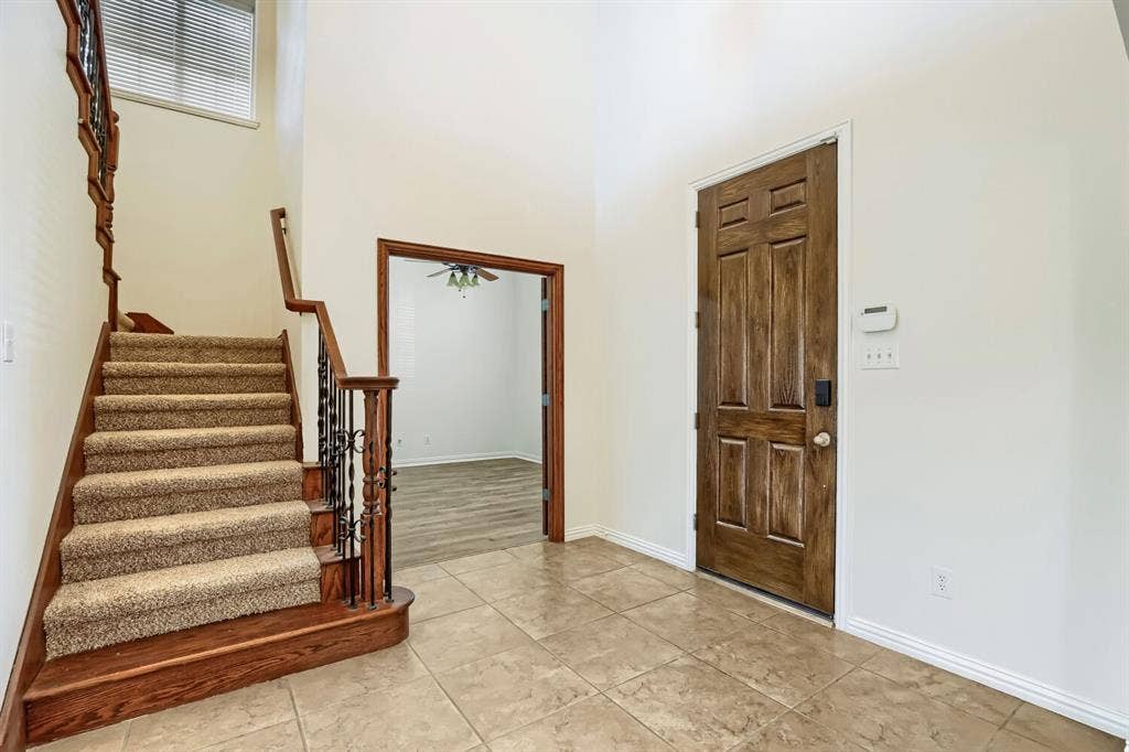7013 Salem Court, Rowlett, TX 75089 Foyer featuring high ceilings, tile flooring, a solid wood-finish entry door, and a staircase with wrought iron balusters and wood-finish railing