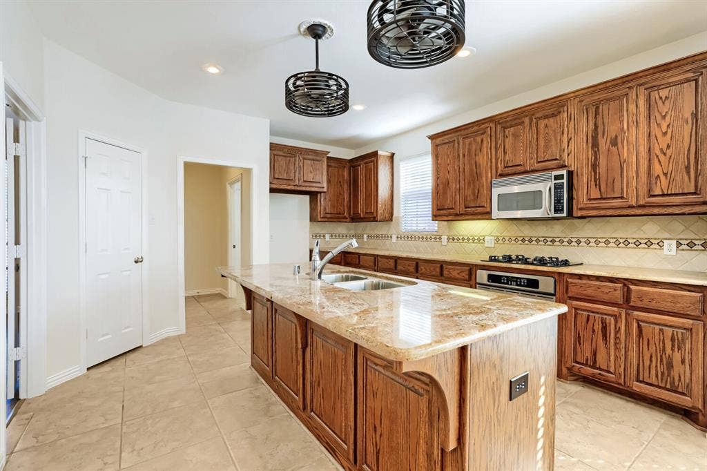 7013 Salem Court, Rowlett, TX 75089 Kitchen featuring custom cabinetry, a central island with a stone countertop, built-in stainless steel appliances, decorative tiled backsplash, and dual cage-style pendant lights