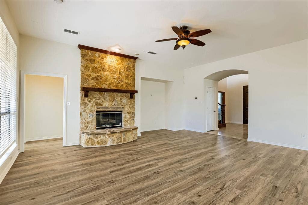 7013 Salem Court, Rowlett, TX 75089 Living area featuring wood-finish flooring, vaulted ceilings, and a floor-to-ceiling stone fireplace with a wooden mantel and raised hearth, complemented by a ceiling fan with integrated lighting