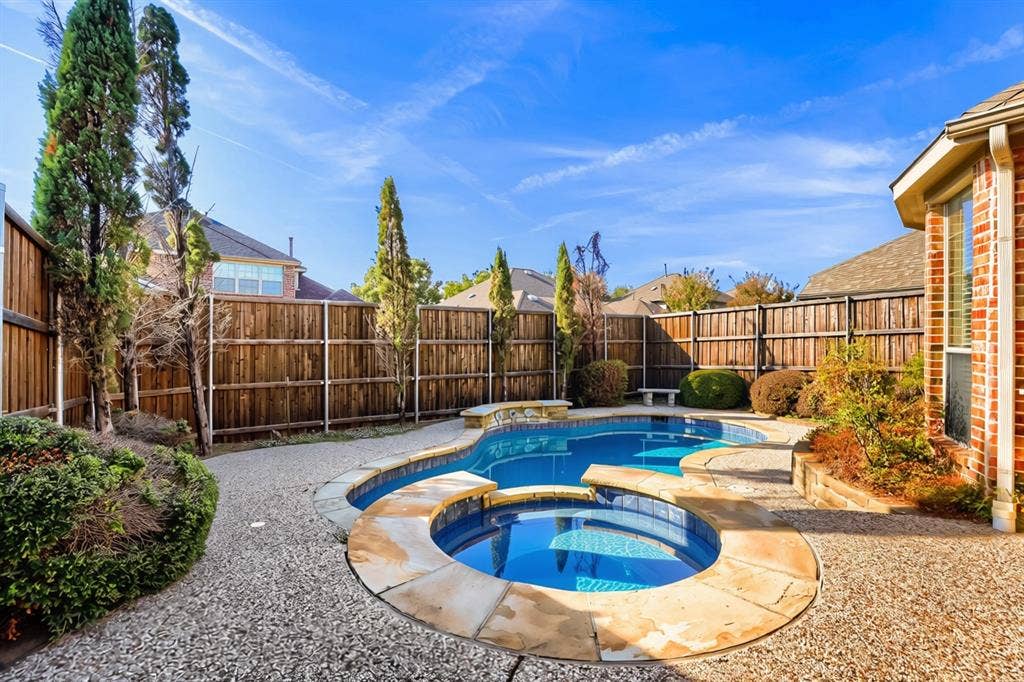 7013 Salem Court, Rowlett, TX 75089 Private backyard featuring an in-ground pool with a spillover spa, natural stone coping, aggregate patio, and wood privacy fencing